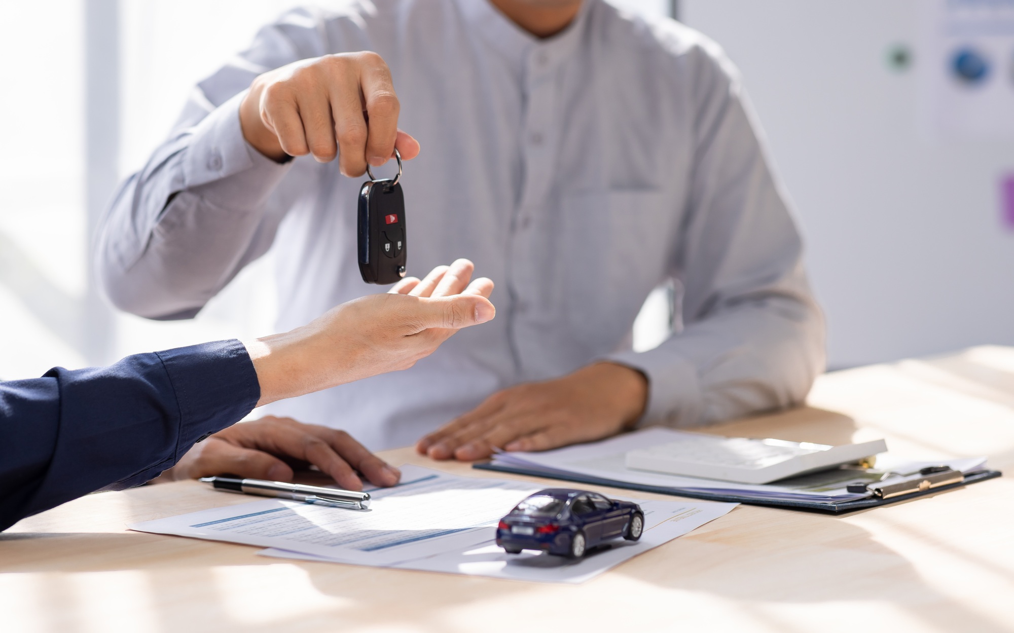 Dealer salesman giving car key to owner. client signing insurance document or rental car lease form