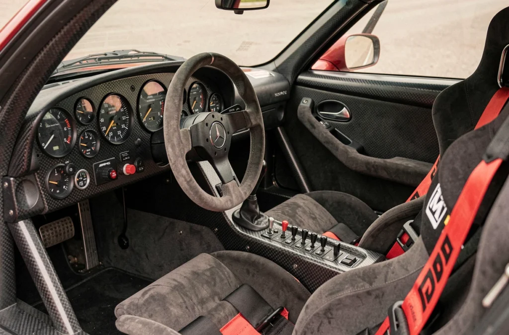 Cockpit intérieur de la Mercedes-Benz CLK GTR avec volant AMG, harnais de course et tableau de bord analogique en fibre de carbone, ambiance supercar racing des années 90